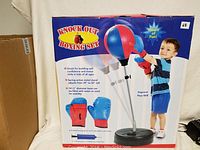 Boxing set in original packaging showing assembled punching ball on adjustable metal stand with base and gloves.