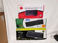 Three new keyboards stacked in original packaging against a white background.
