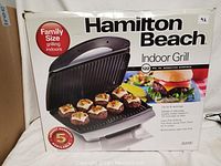 Box front showing Hamilton Beach Family Size Indoor Grill with food on the grill and burger illustration