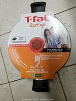 Top side view of the wok packaging showing brand T-Fal, Start Up series, and product features print including non-stick, resistant surface and compatible cooktops.