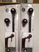 Two packaged drapery rod sets showing rods with spherical finials and hardware in distressed white cards