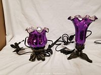 Photo of the two purple glass table lamps with ruffled edges and metal bases with angel figurines, showing cords.