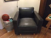 Front view of one deep green leather club chair in room with basketball and wooden floor.