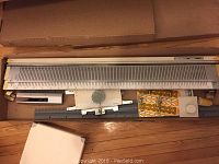 Overview of Singer SR155 Ribber chunky knitting machine accessory in box, showing length and main body with numbered sections and dials.