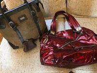 Two handbags pictured on a tan textured fabric; one cork handbag with black trim and attached small cork change purse, one shiny dark red patent leather handbag with handles.