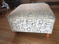Front angled view of square stool ottoman showing geometric pattern upholstery and wooden legs.