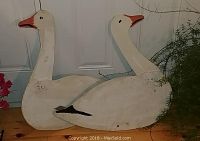 Photo showing two vintage plywood snow geese silhouettes painted white with orange beaks and black eyes, both have ground rods attached for outdoor placement.