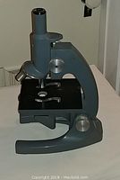 Side view of Bausch and Lomb microscope showing sturdy cast metal construction, adjustable focus knobs, and stage plate with specimen holder clips.