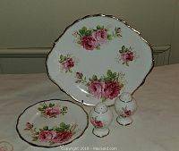 Trio items displayed together: serving plate, dessert plate, salt and pepper shakers with floral pink rose design and gold trim