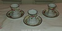Set of three antique hand painted Nippon Co-Co cups with matching saucers, displayed on a beige surface.