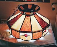 Photo showing amber, honey, cream, and red stained glass hanging fixture with geometric pattern, octagonal shape, placed on a white cloth.