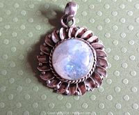 Front view of vintage sterling silver pendant featuring round rainbow moonstone cabochon in decorative floral/sunburst frame with bail.