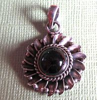 Front close-up photo of the pendant showing the round dark garnet cabochon set in a braided and beaded sterling silver frame.