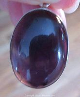 Close-up of the front of the dark amethyst pendant showing the polished cabochon stone in purple hues with a silver bezel setting.
