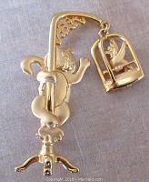Front view of gold-tone brooch showing cat climbing pole and hanging bird cage with bird inside.