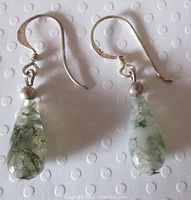Close-up image of vintage sterling silver moss agate dangling pierced earrings lying on a white dotted surface, showing ear wires, silver beads and moss agate teardrop stones.