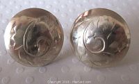 Close-up view of the front of the earrings showing detailed engraved floral or scroll patterns on round silver surfaces.