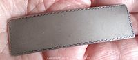 Front side of the rectangular hair clip showing flat surface and edge etching, held in hand for size reference.