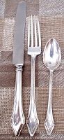 Photo of vintage sterling silver knife, fork, and spoon laid out side by side showing detailed handles and blade