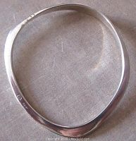 Full view of an irregular, flattened sterling silver bangle bracelet showing its shape and surface condition.