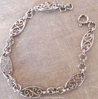 Photo of vintage sterling silver bracelet with open work oval links and spring ring clasp laid flat on beige fabric background