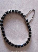 Top view of black facetted square glass stones in silver tone etched frames forming the bracelet with safety chain visible.