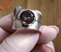 Close-up view of silver ring held in hand showing round smoky quartz stone and curved band with patina.