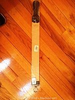 Photo showing the Rite Edge Honing Strip in its original packaging, a slim rectangular strip with black handle and cardboard backing on a wooden floor.