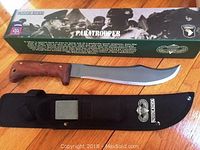 Paratrooper Bowie knife displayed out of the sheath with sharpening stone and original box visible, highlighting wooden handle and curved blade.