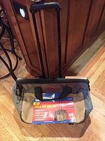 Front view of Storehouse Roll-A-Way Tool Bag with label and extended telescoping handle visible, showing beige and gray fabric and black trim.
