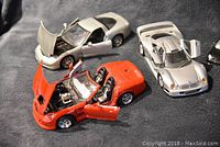 Three metal scale model cars displayed on black fabric, showing doors and hoods open on red convertible and silver coupe, gull-wing doors open on silver sports car