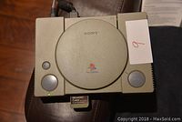 Top view of beige Sony PlayStation console with memory card inserted, green power light visible
