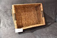 Rectangular wicker basket seen from angled side view showing shape, construction, and handle reinforcements.