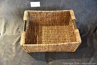 Top view of rectangular wicker basket showing woven texture and black handles on short sides.