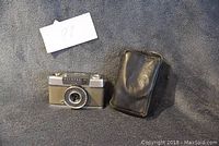 Image of Olympus Pen-EE camera and black leather case on grey fabric background, showing front and side of camera.