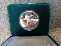 Top view of 1988 Calgary Olympic silver dollar coin inside green velvet display case showing figure skater design.