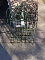 Five green metal garden border fence panels stacked together on pavement, showing arch-topped design and construction.