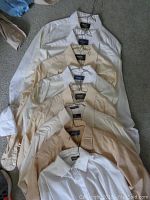 Top view of 7 folded men's Arrow dress shirts in beige, white, cream and light yellow shades, showing collars and buttons.