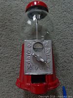Front view of the red gum ball machine showing the clear globe, silver coin mechanism with leaf decoration, and red base and top.
