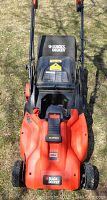 Front view of orange and black Black & Decker cordless mower showing battery cover and attached grass bag