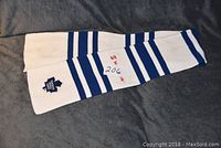 Full view of the white scarf with multiple blue horizontal stripes and embroidered Toronto Maple Leafs logo on one end.