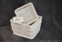 Two white wicker baskets with the smaller nested inside the larger, showing size and shape.