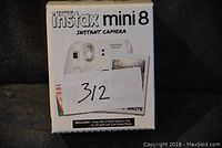 Box of Fujifilm Instax Mini 8 Instant Camera in white with packaging front view, label with lot number covering part of the box.