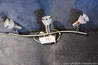 Photo of the brushed nickel ceiling light fixture with three LED bulbs arranged on a slightly curved metal bar against a dark background.