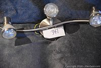 Curved brushed nickel ceiling fixture with three LED bulbs, displayed on a dark blue cloth background, with a label number 347 underneath.