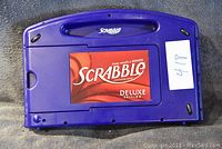 Closed dark blue plastic carrying case with Scrabble Deluxe Edition label on front.