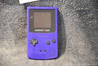Front view of the purple Nintendo Game Boy Color handheld console with visible screen, buttons, and speaker grill.