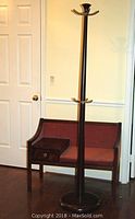 Full view of the wooden coat rack next to the wooden telephone bench with mauve upholstery.