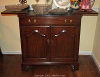 Front view showing cabinet doors, single drawer, brass handles and caster base