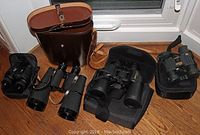 Four pairs of binoculars with cases displayed on wooden floor